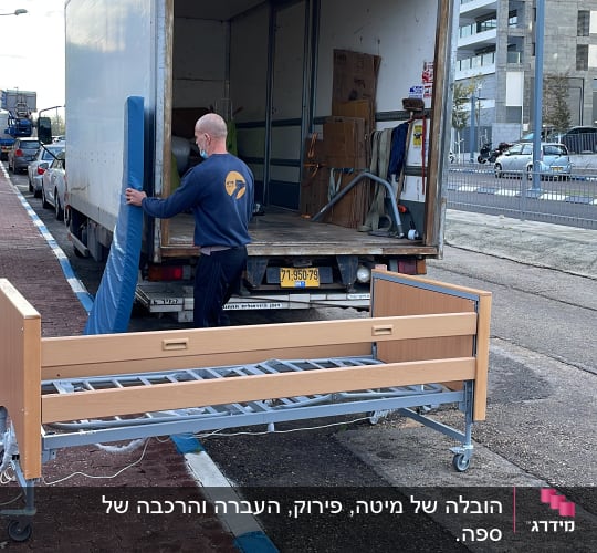 אדם מעמיס מיטה למשאית הובלה ברחוב עירוני